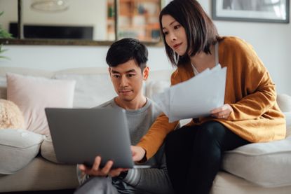 Two people looking at a laptop with paperwork in hand