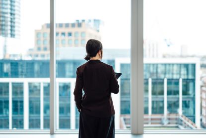 Businessperson with digital tablet, standing against office window with city view